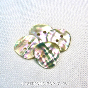 May include: Four iridescent shell buttons with two holes each, arranged on a white textured surface. The buttons display a range of colors, including green, pink, and gold. The text at the bottom reads "4 BUTTONS FOR $3.20".