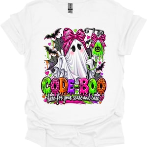Può includere: Una t-shirt bianca con la grafica di un fantasma che indossa un fiocco rosa, che regge un'asta per flebo con una sacca di liquido verde. Il testo recita CODE-BOO e here for your scare and care, circondato da pipistrelli, ragnatele e cuori neon.