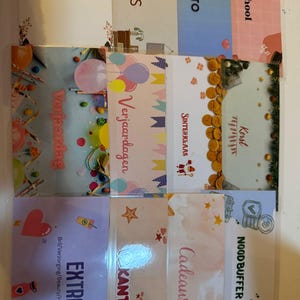 Puede incluir: Una colección de sobres de presupuesto coloridos con varios temas. Los sobres están etiquetados con palabras como "Escuela", "Extra" y "Regalos". El diseño incluye ilustraciones de globos, galletas y otros elementos decorativos.