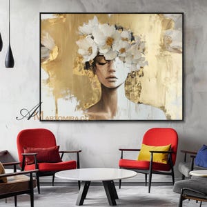 Puede incluir: Pintura abstracta de una mujer con los ojos cerrados, adornada con una corona de flores blancas. El fondo presenta pinceladas doradas y blancas. La obra está enmarcada en negro y cuelga sobre sillas rojas y una mesa blanca.