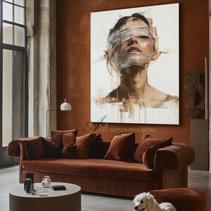 May include: An abstract painting of a person with their eyes covered in white bandages. The artwork is displayed above a brown velvet sofa with matching throw pillows. The room has a modern design with a round coffee table.