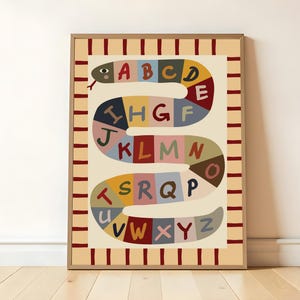 Könnte beinhalten: Ein gerahmter Wandkunstdruck mit einer gewundenen Schlangenillustration, die aus farbigen Segmenten besteht, von denen jedes einen Buchstaben des Alphabets von A bis Z enthält. Der Rand hat einen cremefarbenen Hintergrund mit dunkelroten Streifen.