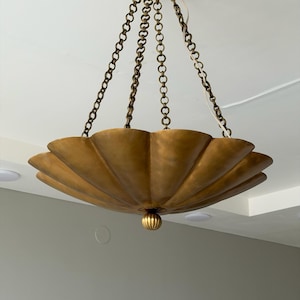 May include: A brass-toned metal pendant light fixture featuring a wide, scalloped, bowl-shaped shade. The fixture is suspended from a circular ceiling canopy by three decorative metal chains and includes a small, ribbed, spherical finial at the base.