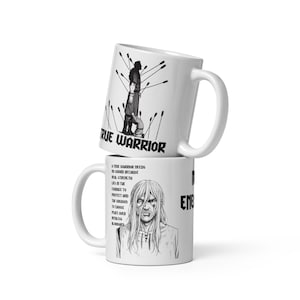 Puede incluir: Dos tazas de cerámica blancas apiladas. La taza superior presenta una figura de guerrero con flechas y el texto "TRUE WARRIOR". La taza inferior tiene un retrato y texto sobre la fuerza y el coraje.