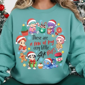 May include: A teal sweatshirt featuring a festive design with anime-style characters wearing Santa hats. The graphic includes text that reads "These are a few of my cozy little Six Boys" surrounded by Christmas-themed illustrations like snowflakes, gingerbread men, and a blue tiger.