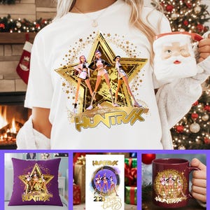 Peut inclure: T-shirt blanc avec une étoile dorée représentant trois personnages et le mot "HUNTRAX" en or. Une tasse du Père Noël est tenue à la main. D'autres articles incluent un coussin violet, une carte de vœux et une tasse marron, tous avec le même design.