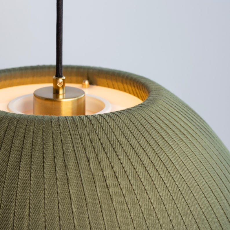 May include: Close-up of a green fabric pendant light fixture. The shade has vertical ribbed detailing. The fixture has a brass-colored metal base and a black cord.