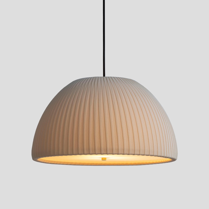 May include: Cream-colored, dome-shaped pendant light fixture. The shade has vertical, ribbed detailing. A black cord suspends the light from above. The interior of the shade glows with a warm light.