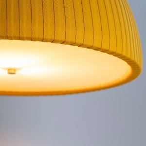 May include: Close-up of a yellow lampshade with a ribbed texture. The lampshade has a rounded shape and a warm, glowing light emanating from within. The color is a vibrant, sunny yellow.