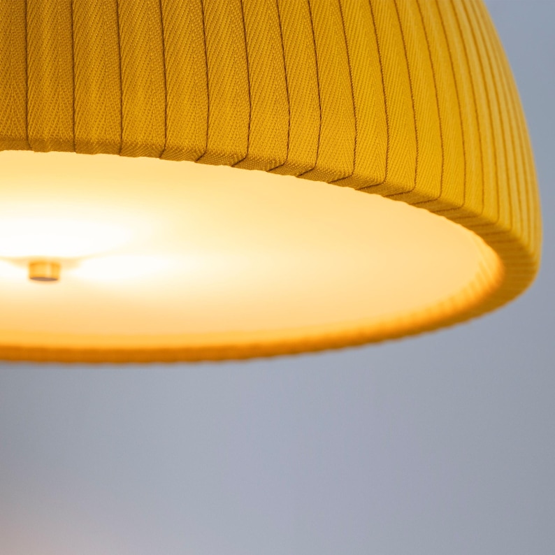 May include: Close-up of a yellow lampshade with a ribbed texture. The lampshade has a rounded shape and a warm, glowing light emanating from within. The color is a vibrant, sunny yellow.