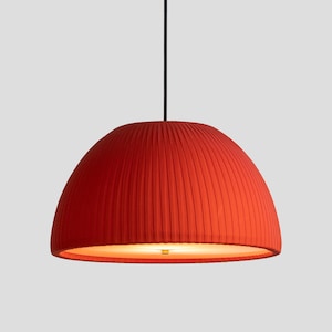 May include: A red pendant light fixture with a pleated, dome-shaped shade. The shade is suspended from a black cord and has a warm, diffused glow from the light source within. The fixture is a modern design.