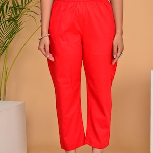 May include: Bright red pants with an elastic waistband. The pants are paired with a black top. The model is wearing a bracelet and ring. The pants are made of a lightweight fabric and have a relaxed fit.