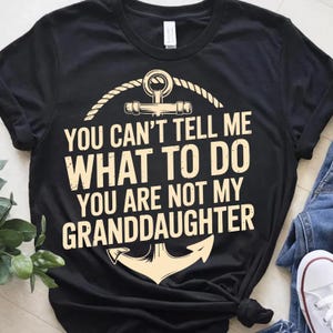 Puede incluir: Camiseta negra con el texto crema "YOU CAN'T TELL ME WHAT TO DO YOU ARE NOT MY GRANDDAUGHTER". El diseño incluye un ancla y detalles de cuerda.