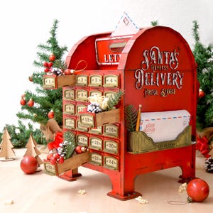Könnte beinhalten: Ein roter Adventskalender in Form eines alten Briefkastens mit der Aufschrift "Santa's Express Delivery" auf der Vorderseite. Er hat 24 nummerierte Schubladen, die mit festlichem Grün und Ornamenten geschmückt sind. Weihnachtsdekorationen umgeben den Briefkasten.