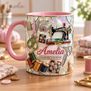 May include: A ceramic mug with a pink handle and interior, featuring a pearlescent finish and a colourful collage of sewing tools including a sewing machine, scissors, spools of thread, buttons, a thimble, and a pincushion, with the name Amelia printed.