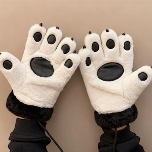 May include: A pair of white plush gloves designed to resemble bear paws. Each glove features black paw pads and claws, with a black cuff. The gloves are connected by a black string.