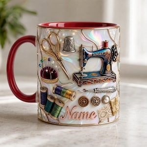 Puede incluir: Una taza de cerámica blanca iridiscente con interior y asa rojos, que presenta ilustraciones en relieve de herramientas de costura, incluyendo una máquina de coser Singer, tijeras, un dedal, carretes de hilo, botones y la palabra Name.