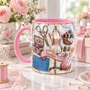May include: A white ceramic mug with a pink interior and handle, featuring an iridescent finish and a sewing-themed design. The print includes a dress form, scissors, a sewing kit, spools of thread, a pincushion, and a banner with the name Sophia.