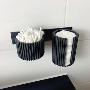 May include: A white ceramic mug with a black handle and the text "But First, Coffee" in a bold, black font. The mug is set against a blurred background, suggesting a cozy setting.