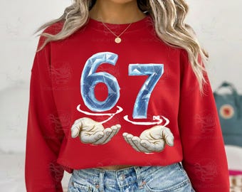 May include: Red sweatshirt featuring the number "67" in a blue, icy font, with hands cupping the numbers. The design is centered on the front of the shirt. The sweatshirt is a solid red color.