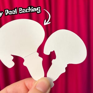 May include: Two white die-cut stickers, shaped like a jellyfish, are held against a bright pink background. The text "Easy Peel Backing" is above the stickers, with an arrow pointing to the top sticker.