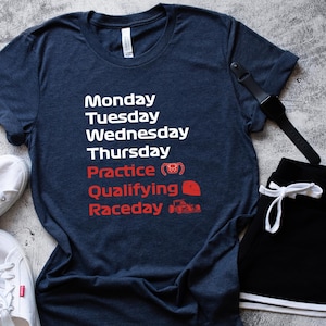 May include: A navy blue t-shirt with white text listing days of the week and racing terms in red. The shirt is paired with black shorts, white sneakers, and a black watch. The text includes "Practice", "Qualifying", and "Raceday".