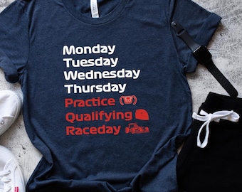 May include: A navy blue t-shirt with white text listing days of the week and racing terms in red. The shirt is paired with black shorts, white sneakers, and a black watch. The text includes "Practice", "Qualifying", and "Raceday".