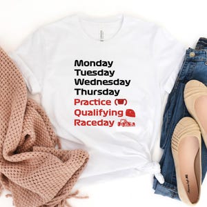 May include: White t-shirt with black text listing days of the week, with "Practice", "Qualifying", and "Raceday" in red. A red race car and a coffee cup graphic are included. The shirt is paired with blue jeans and tan flats.