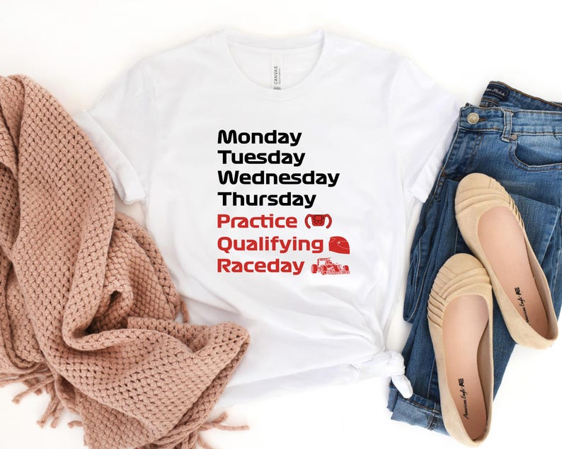 May include: White t-shirt with black text listing days of the week, with "Practice", "Qualifying", and "Raceday" in red. A red race car and a coffee cup graphic are included. The shirt is paired with blue jeans and tan flats.