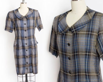Puede incluir: Un vestido de cuadros con cuello y mangas cortas. El vestido tiene un cierre de botones en la parte delantera y dos bolsillos en la parte delantera.