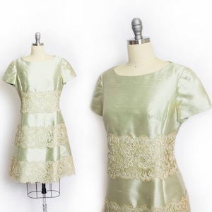 May include: A light green dress with a lace trim and a layered skirt. The dress has short sleeves and a fitted bodice.