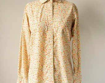 Puede incluir: Una camisa blanca de botones con un pequeño estampado floral en tonos naranja, amarillo y verde.