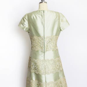May include: A light green dress with a fitted bodice and a flared skirt. The dress is made of a silky fabric and features delicate lace trim around the neckline, waist, and hem.