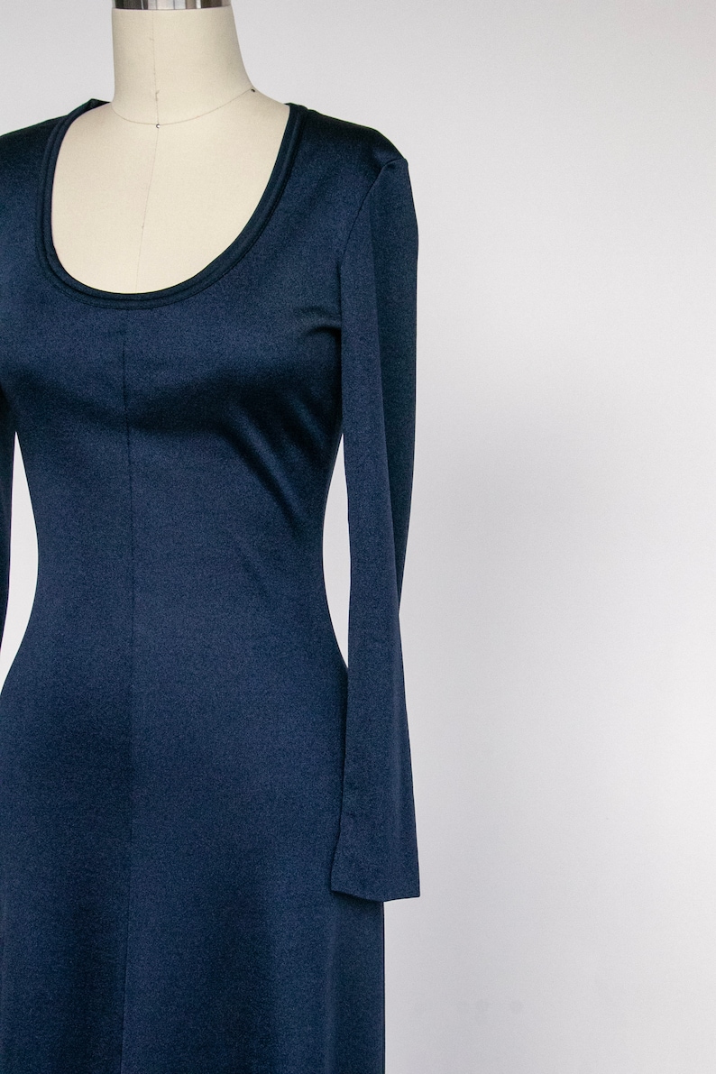 Puede incluir: Un vestido largo de manga larga de color azul marino con escote redondo. El vestido est&aacute; ajustado en el cuerpo y se ensancha ligeramente en la falda.