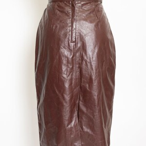May include: A brown leather pencil skirt displayed on a mannequin. The skirt has a high waist with a button closure and a back slit. The leather has a slightly wrinkled texture.