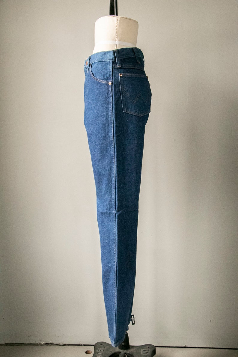 Puede incluir: Un par de pantalones vaqueros azules de mezclilla en un maniqu&iacute;. Los pantalones tienen una pierna recta y un dise&ntilde;o cl&aacute;sico de cinco bolsillos.
