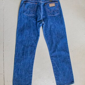 May include: A pair of blue denim jeans with a brown leather patch on the back pocket that says "Wrangler".