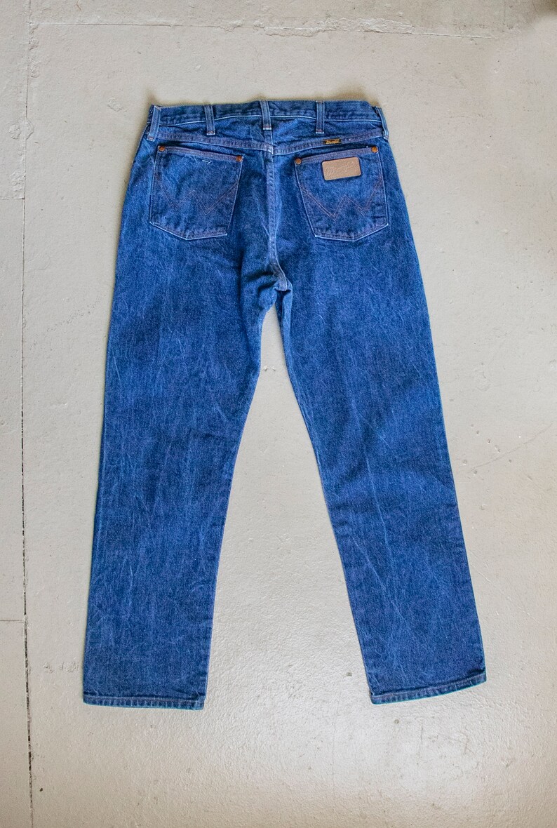 May include: A pair of blue denim jeans with a brown leather patch on the back pocket that says "Wrangler".