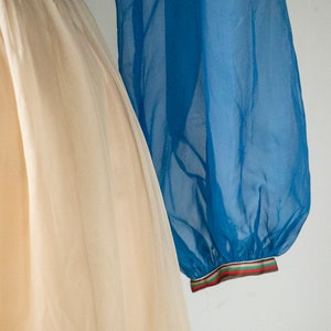 May include: A white tulle skirt with a blue sheer overlay. The overlay has a colorful ribbon trim.
