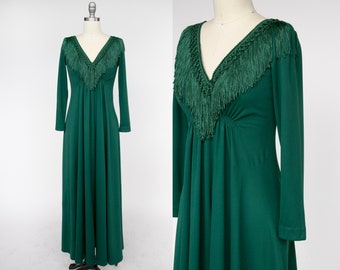 Puede incluir: Un vestido largo de maxi verde oscuro con escote en V y mangas largas. El escote está adornado con un detalle de flecos.