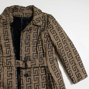 May include: A long brown quilted coat with a black geometric pattern. The coat has a black fur lining, a belt, and two buttons.