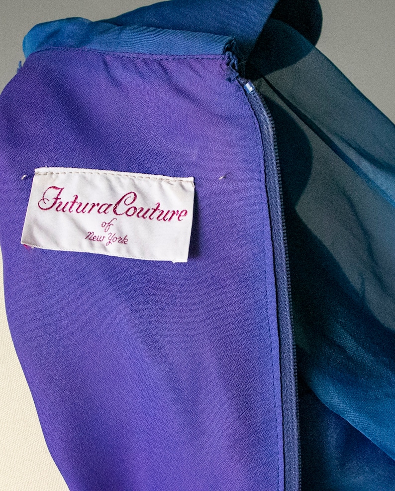 May include: A purple and blue dress with a zipper closure and a white label that reads "Futura Couture of New York".