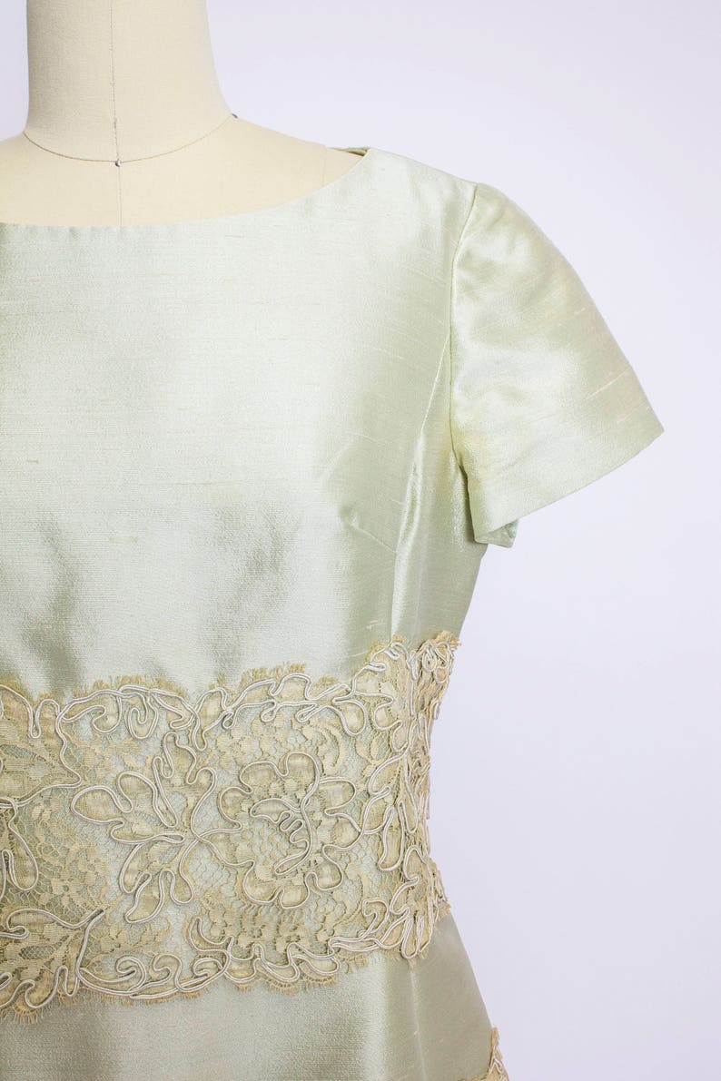 May include: A light green dress with a lace trim around the waist. The dress has short sleeves and a scoop neck.