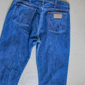 May include: A pair of blue denim jeans with a brown leather patch on the back pocket that says "Wrangler".