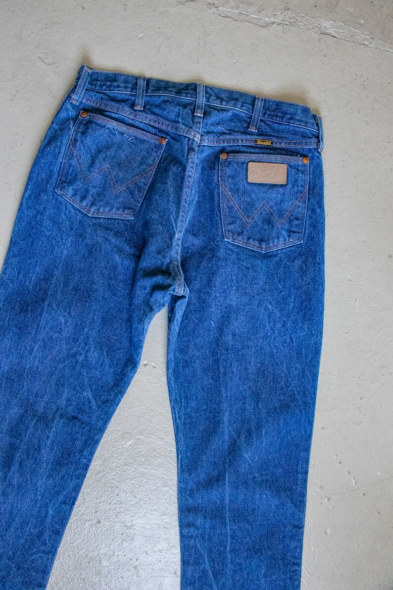May include: A pair of blue denim jeans with a brown leather patch on the back pocket that says "Wrangler".
