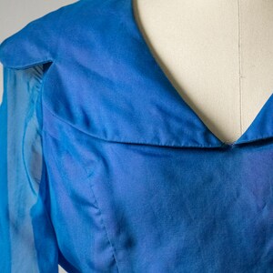 May include: A blue sheer blouse with a V-neck and long sleeves. The blouse has a collar that folds down and a gathered detail at the neckline.