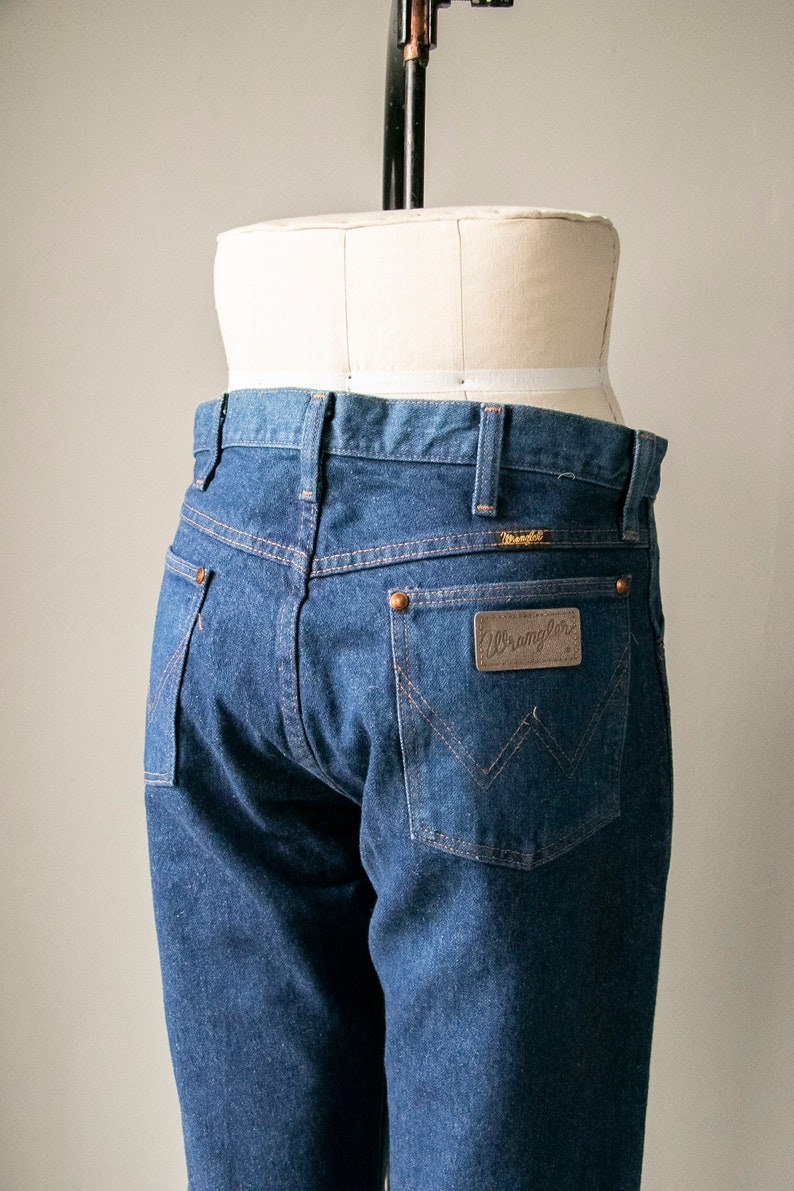 Puede incluir: Un par de pantalones vaqueros azules con un parche de cuero marr&oacute;n de Wrangler en el bolsillo trasero.