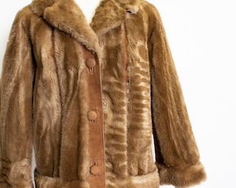 May include: A brown faux fur jacket with a suede panel down the front and four brown buttons. The jacket has a collar and long sleeves with brown faux fur cuffs.
