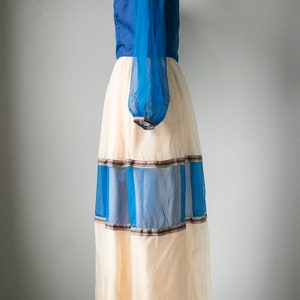 May include: A long, flowing dress with a blue bodice and a sheer, cream-colored skirt. The skirt has blue and brown stripes around the hem.