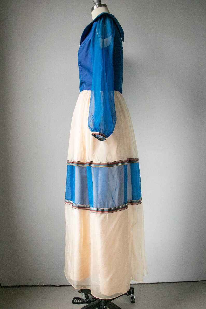 May include: A long, flowing dress with a blue bodice and a sheer, cream-colored skirt. The skirt has blue and brown stripes around the hem.